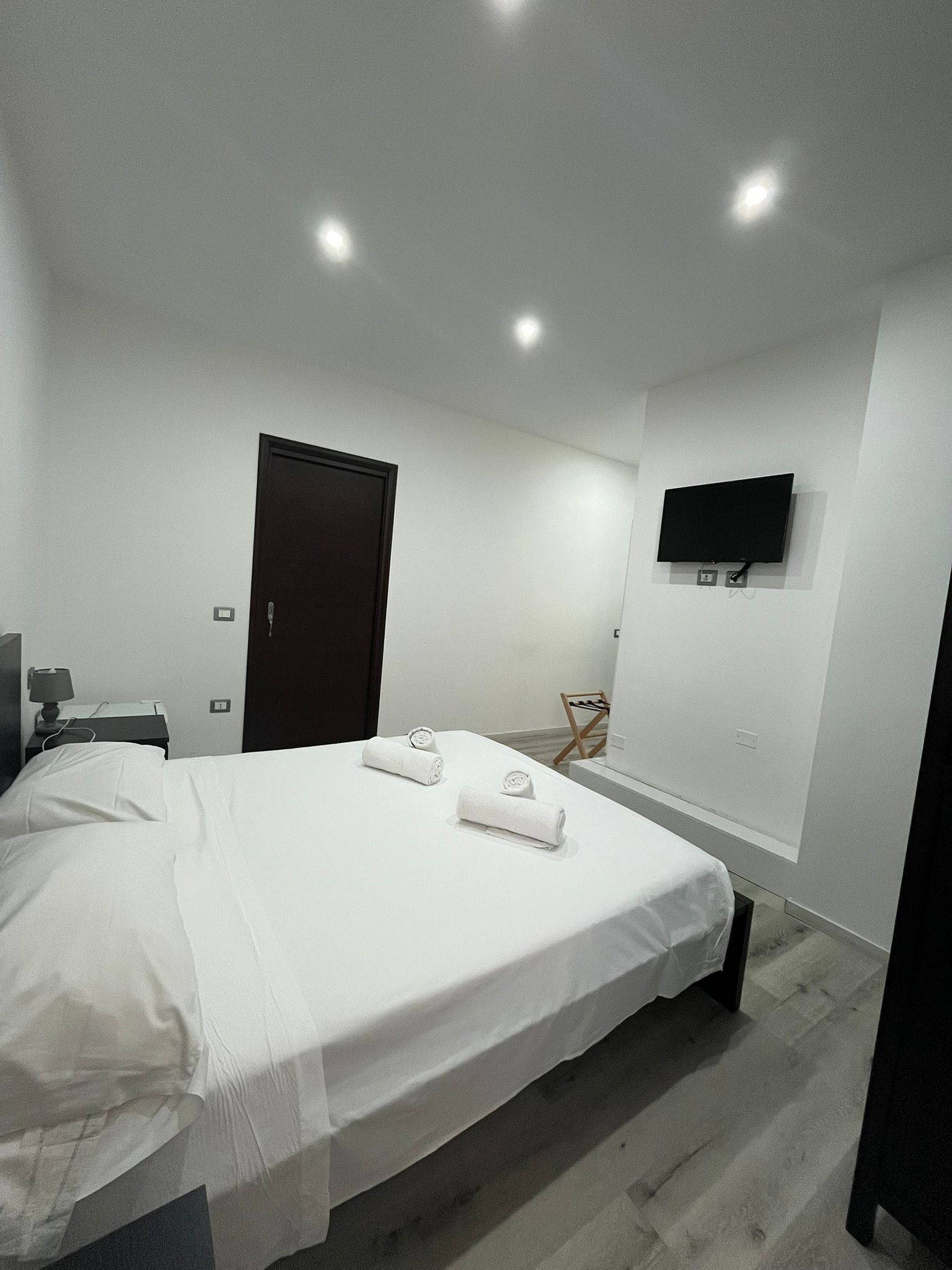 A modern hotel room with a large bed, a flat-screen TV mounted on the wall, and a wooden floor.
