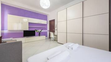 A hotel room with a bed, a desk, a chair, a TV, and a wardrobe.
