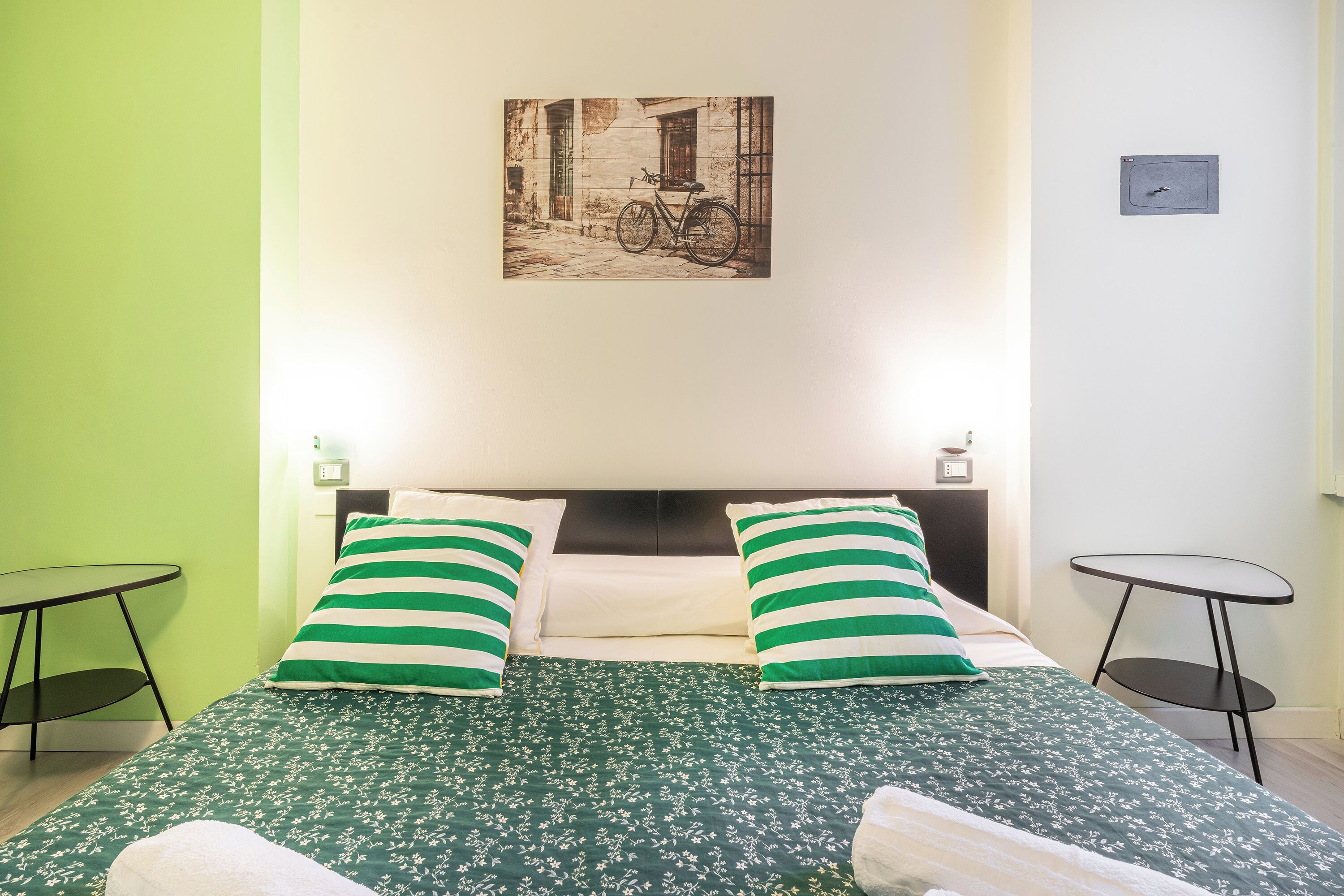 Ein Hotelzimmer mit einem Bett, zwei Kissen, einem Kopfteil, einem kleinen Tisch und einem an der Wand hängenden Bild.