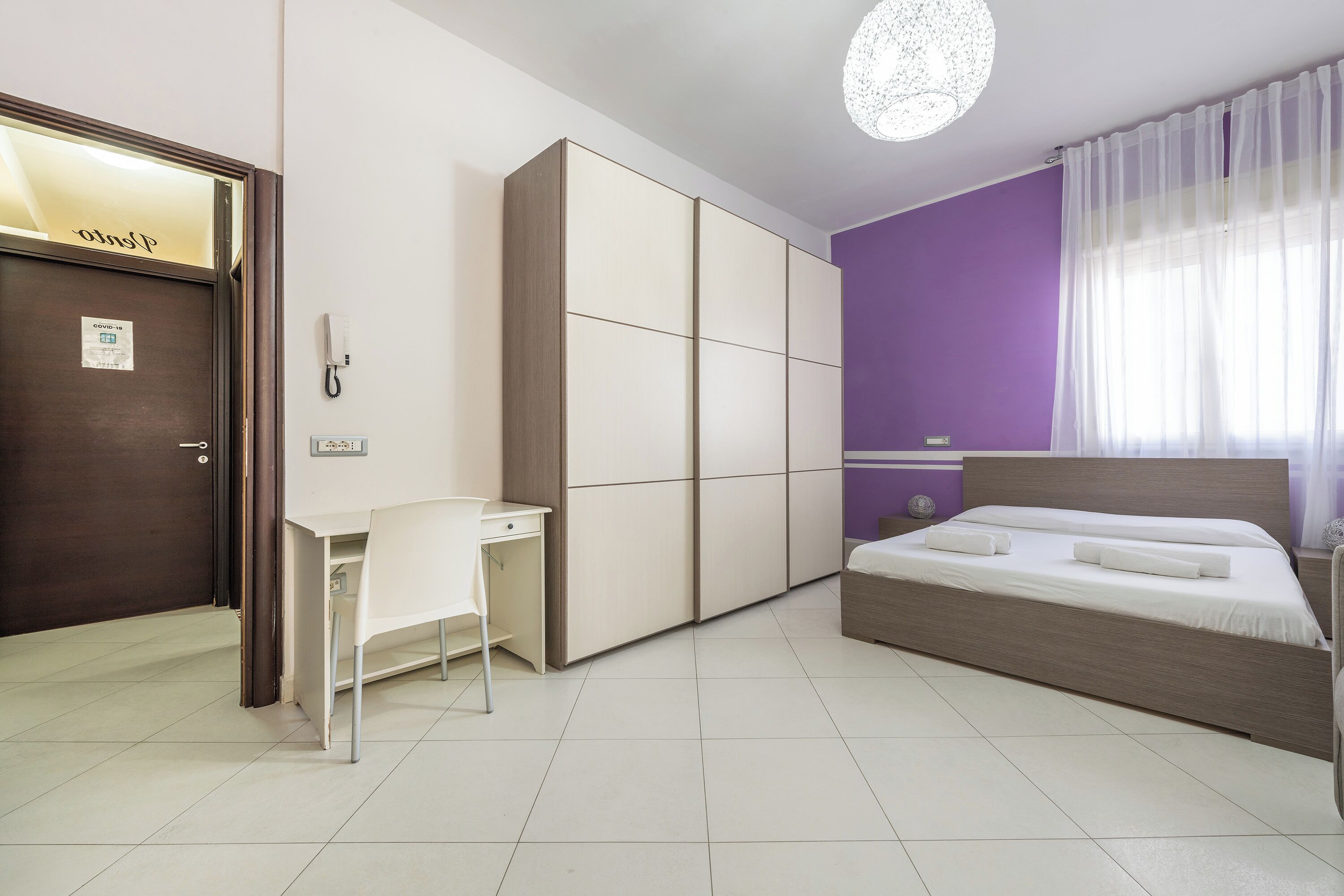 A bedroom with a bed, a desk, and a wardrobe.