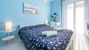 Una camera da letto con un letto, un comodino, una lampada, una sedia, una scrivania, un vaso con fiori e una finestra con tende.