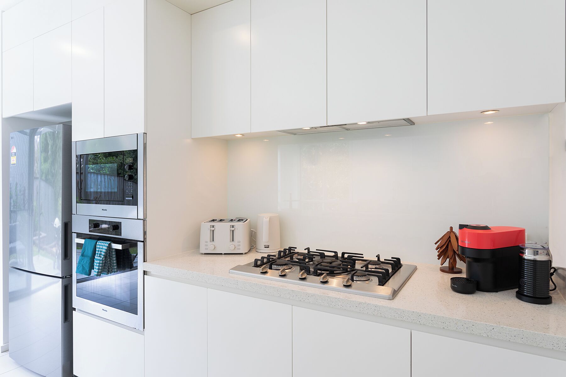 Una cucina moderna con mobili bianchi, forno a incasso, piano cottura a gas, tostapane e macchina per il caffè.