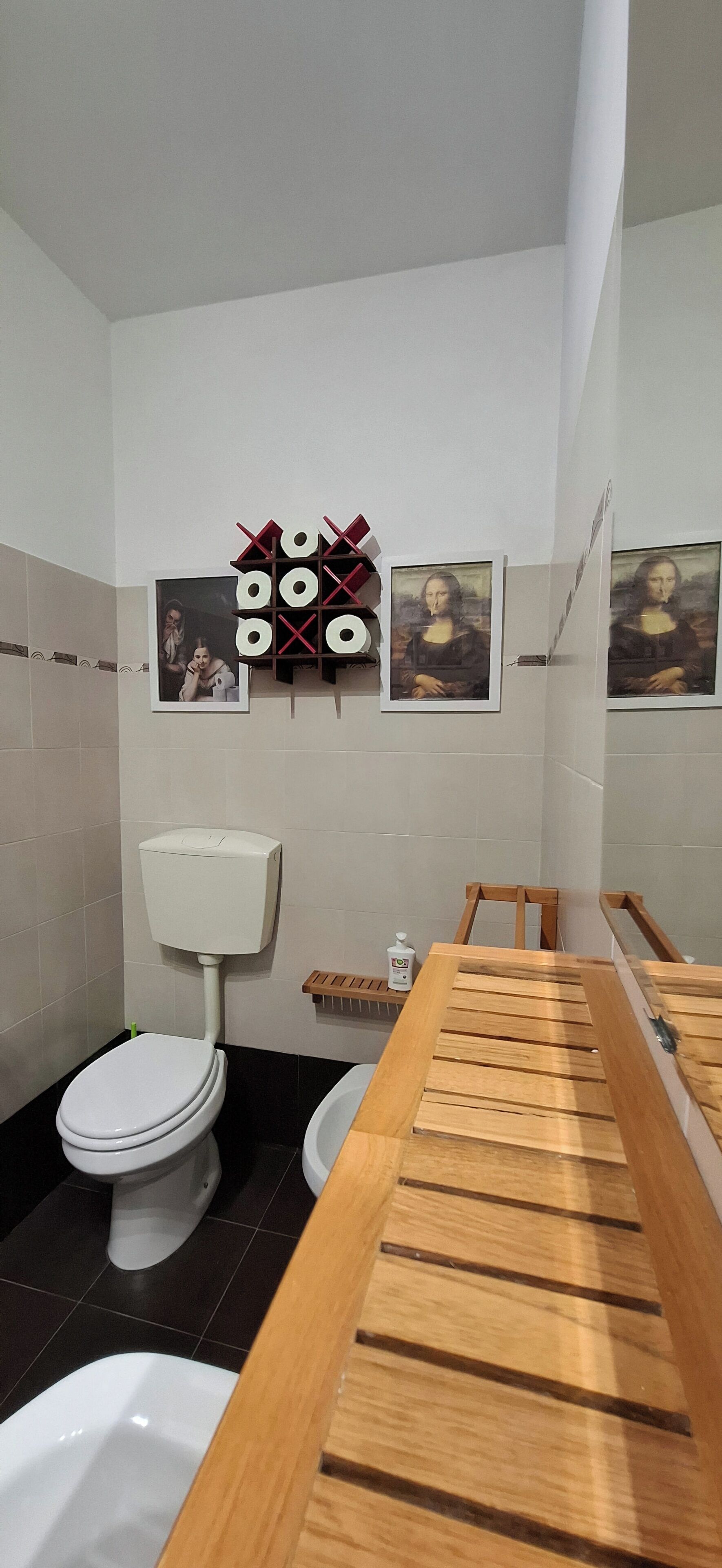 A bathroom with a wooden vanity, a toilet, and two framed pictures on the wall.