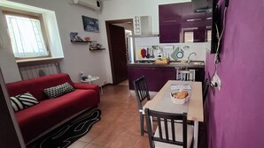 A compact living space with a red sofa, a dining table with chairs, a kitchen area with purple cabinets, and a small side table. - Vacation House "al Vicoletto" (Pratola Peligna)