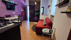 A compact kitchen with a gas stove, a dining table with chairs, and a red sofa. A small table with a book and a cup is next to the sofa. - Vacation House "al Vicoletto" (Pratola Peligna)