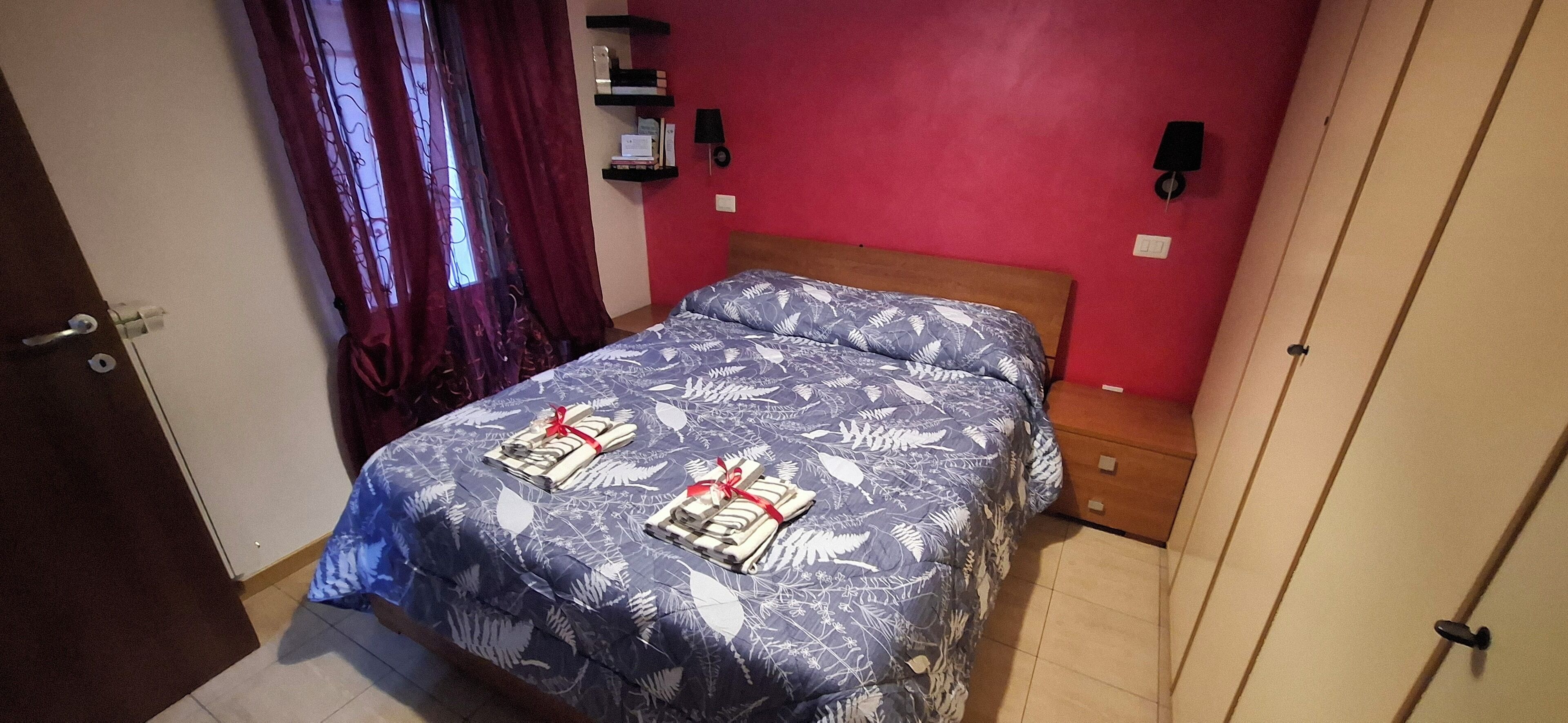 A bedroom with a bed, a nightstand, a red wall, and a door.