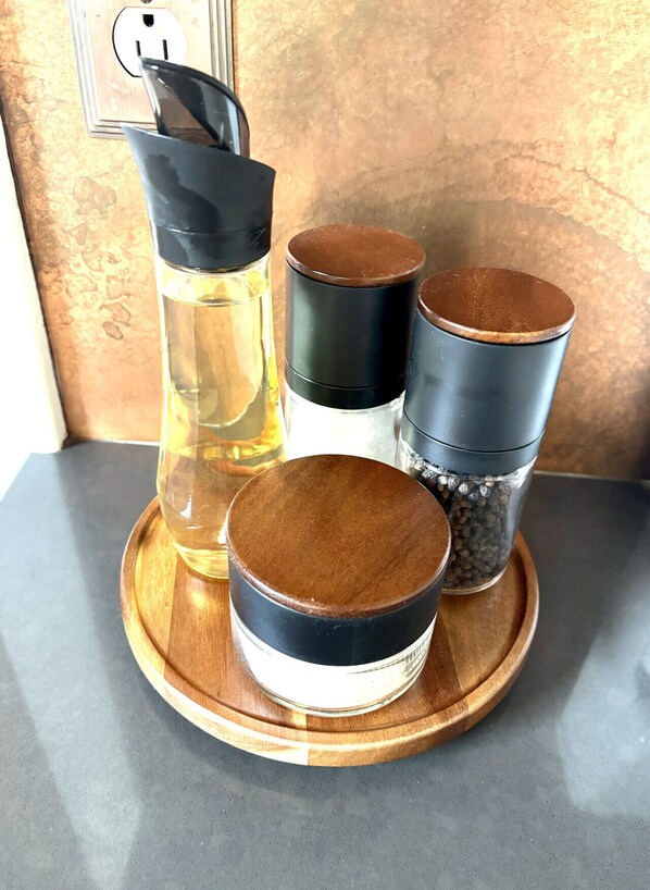 Un plateau en bois sur lequel se trouvent une bouteille contenant un liquide, deux récipients munis de couvercles et un petit bol, le tout posé sur un comptoir.