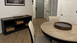 Un coin repas comprenant une table ronde, des chaises, une console en bois foncé agrémentée de paniers et un tableau encadré accroché au mur.