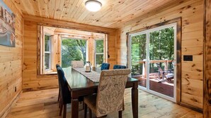 A wooden cabin with a dining area, large windows, and a sliding glass door leading to an outdoor deck. - Willow Falls (Blue Ridge)