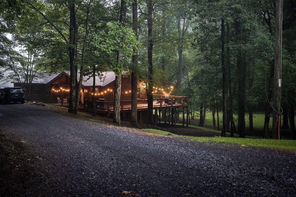 A cabin with a deck, surrounded by trees, and string lights.