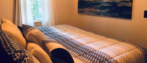 Une chambre à coucher avec un lit, des oreillers, une fenêtre avec des rideaux et un tableau au mur.