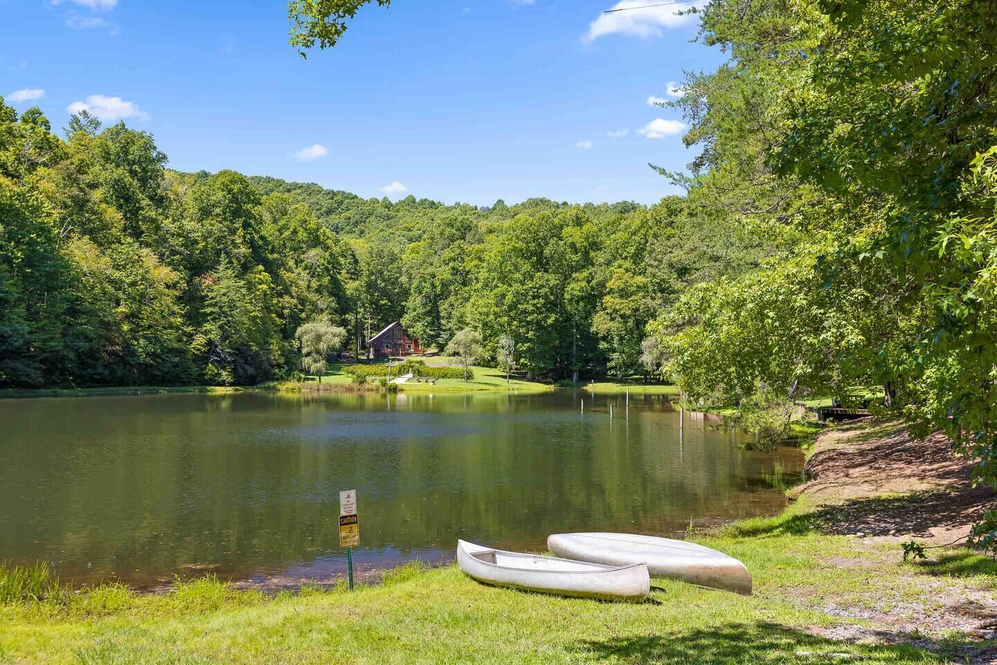 A serene lakeside scene with a cabin, boats, and lush greenery.