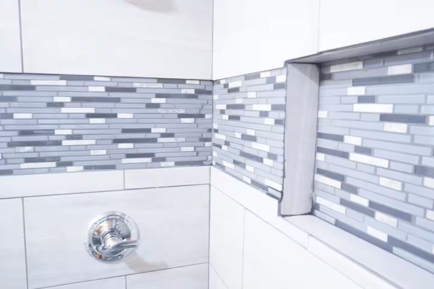 A corner of a bathroom with a modern tiled backsplash and a chrome sink.