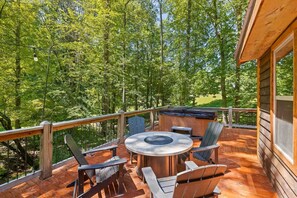 Een houten terras met een jacuzzi, zitplaatsen buiten en uitzicht op een bos.