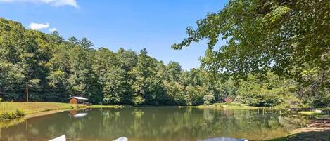 A serene lakeside setting with a canoe and a paddle resting on the grass, surrounded by lush greenery and a clear sky.