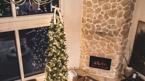 Un salon chaleureux avec une cheminée en pierre, un sapin de Noël et des fauteuils confortables.