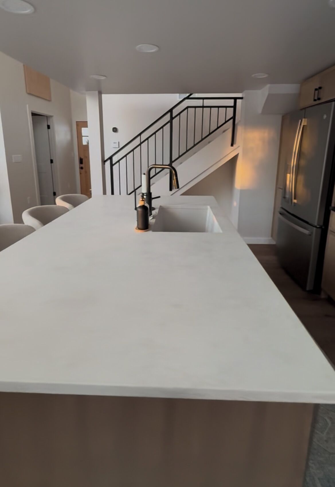 Una cocina moderna con una isla central, electrodomésticos de acero inoxidable y una escalera que sube a otro nivel.