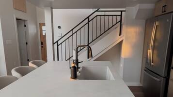 Una cocina moderna con una isla central, electrodomésticos de acero inoxidable y una escalera que sube a otro nivel.