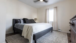 A bedroom with a bed, a ceiling fan, a nightstand, a dresser, and a window with curtains. - Private Modern 3 Bed Apt Close to Downtown- 1st Flr (Torrington)