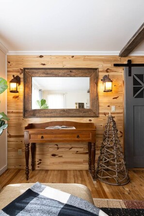 Pared de madera con un espejo grande, una consola de madera y dos faroles fijados a la pared.