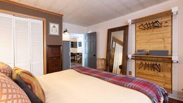 Quarto com cama, guarda-roupa, espelho e parede de madeira com roupas penduradas.