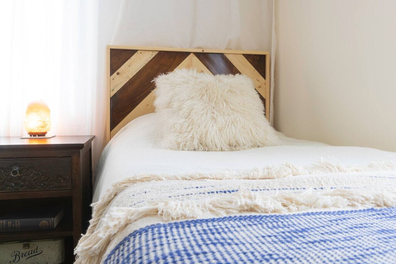 A bed with a white fluffy pillow, a blue and white checkered blanket, and a wooden headboard with a chevron pattern.