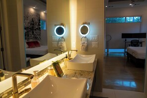 A modern bathroom with two sinks, a large mirror, and a bedside table. - Elysian Haven - Modern Urban Oasis in a Peaceful Neighborhood (San Antonio)