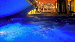 Une piscine éclairée de lumière bleue, un espace extérieur aménagé et couvert, et un bâtiment en arrière-plan.
