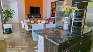Une cuisine moderne dotée d’un plan de travail en marbre, d’appareils électroménagers en acier inoxydable et d’un coin repas avec des chaises blanches et une table aux couleurs vives.