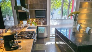 A modern kitchen with a gas range, stainless steel appliances, and a view of trees outside. - Elysian Haven - Modern Urban Oasis in a Peaceful Neighborhood (San Antonio)