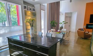 A modern kitchen with a large island, high ceilings, and a dining area with a plant. - Elysian Haven - Modern Urban Oasis in a Peaceful Neighborhood (San Antonio)