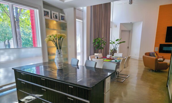A modern kitchen with a large island, high ceilings, and a dining area with a plant. - Elysian Haven - Modern Urban Oasis in a Peaceful Neighborhood (San Antonio)