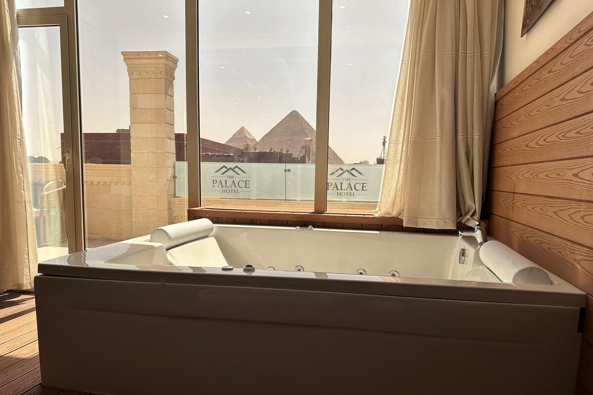 A modern bathroom with a large bathtub, a wooden wall, and a view of the pyramids through a window.