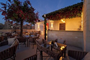 An outdoor seating area with wicker furniture and a tree, a brick wall with a door, and warm lighting. - Ra Palace Pyramids View (Giza)