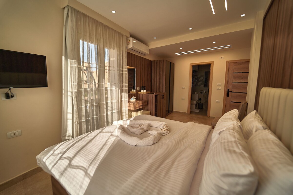 A modern bedroom with a large bed, a TV mounted on the wall, and a walk-in closet.