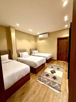 A hotel room with three beds, a wooden floor, a patterned rug, and an air conditioning unit on the wall. - Ra Palace Pyramids View (Giza)