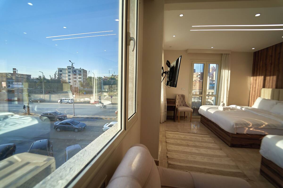 A hotel room with a large window, a bed, a desk, and a chair.