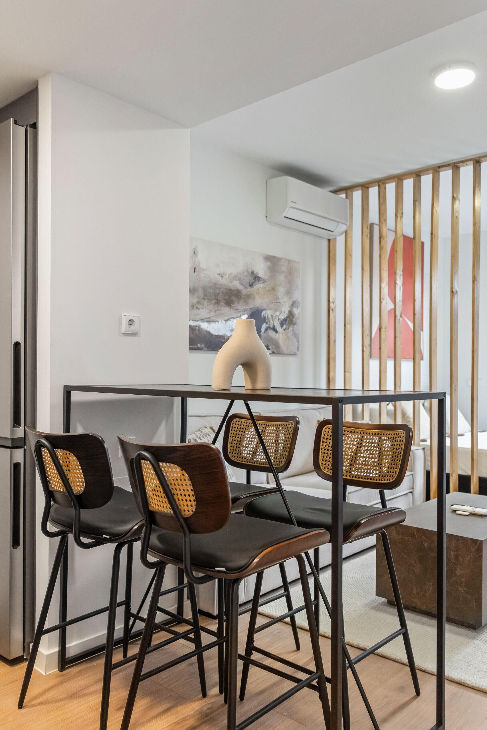 A modern kitchen with a dining area, featuring a refrigerator, a table with chairs, and an air conditioning unit on the wall.