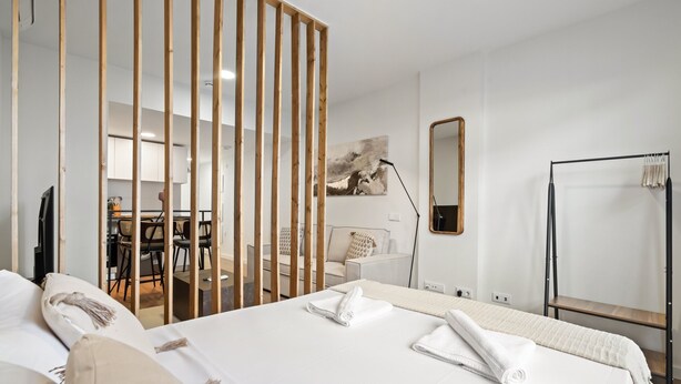 Ett hotellrum med en stor säng, en trävägg som avskärmning, ett skrivbord med stolar, en spegel och en garderob.
