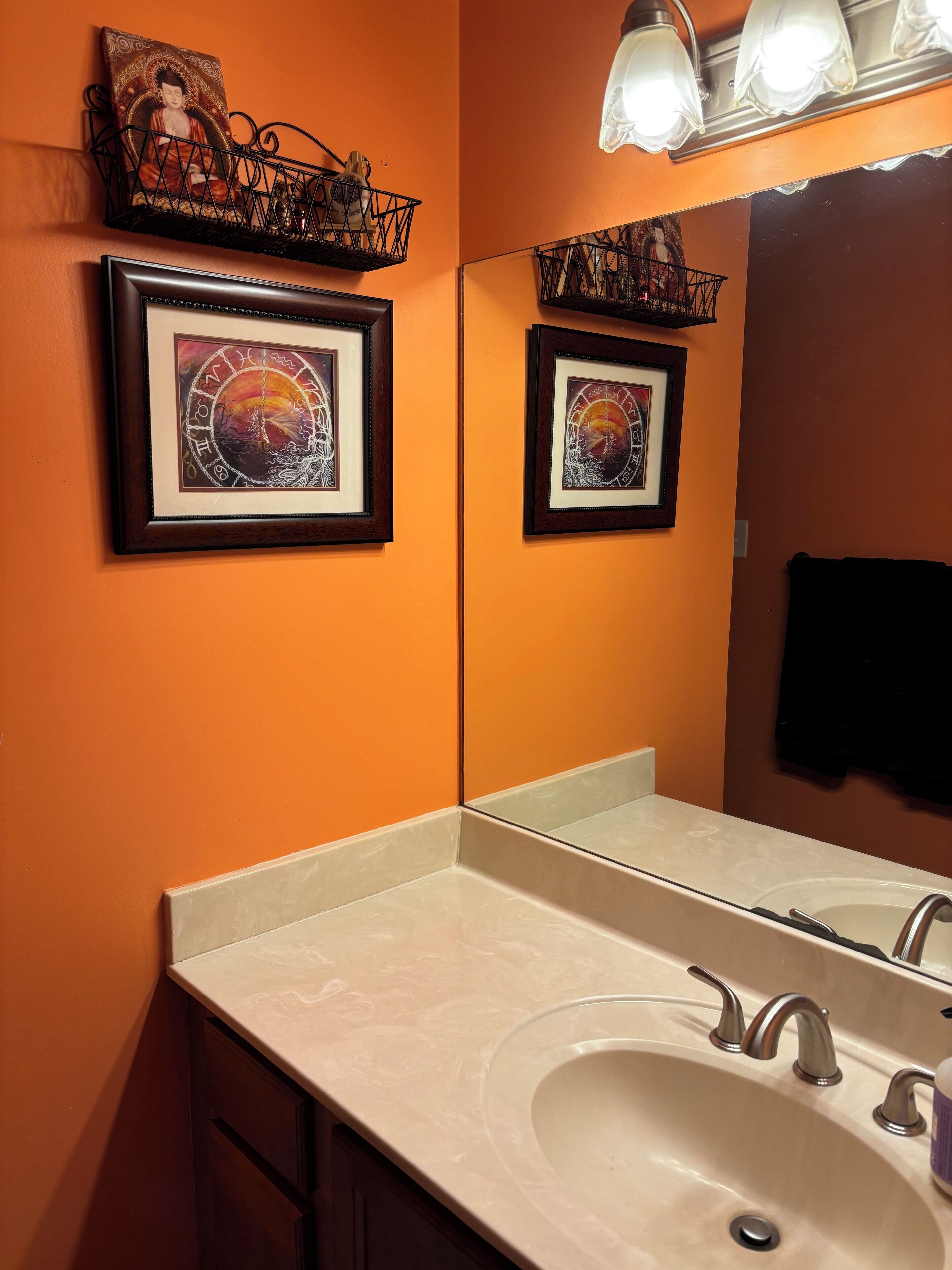 A bathroom with a double sink, framed artwork above the mirror, and a light fixture above the mirror.
