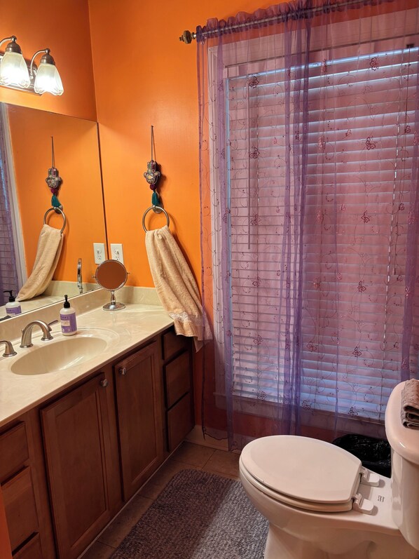 Un baño con pared naranja, un lavabo con espejo, un inodoro y una cortina de ducha con motivos florales.