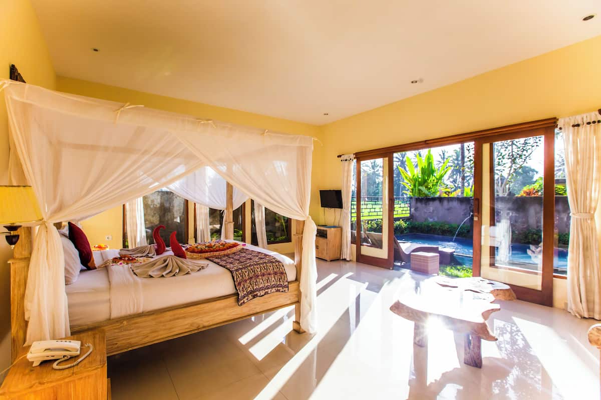 A bedroom with a four-poster bed, a bedside telephone, and a view of a garden through large glass doors.