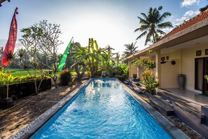 A swimming pool with a tiled edge, surrounded by palm trees and plants. - Asri Sari Villa Ubud (Ubud)