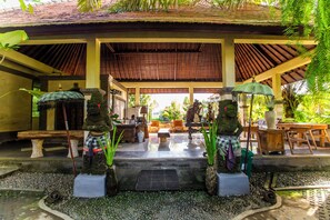 A covered outdoor area with stone statues, wooden furniture, and a tiled floor. - Asri Sari Villa Ubud (Ubud)
