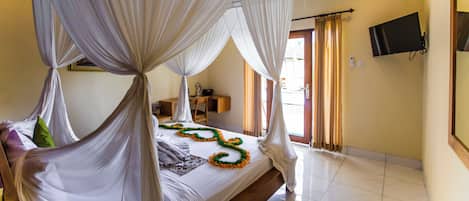 A four-poster bed with sheer curtains, a flat-screen TV mounted on the wall, and a view of the outside through a door.