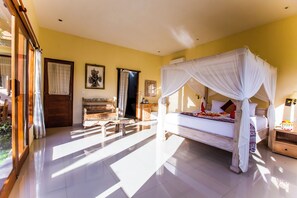 A spacious bedroom with a canopy bed, a wooden bench, and a nightstand with a lamp. - Asri Sari Villa Ubud (Ubud)