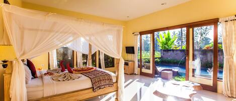 A bedroom with a four-poster bed, a bedside telephone, and a view of a garden through large glass doors.