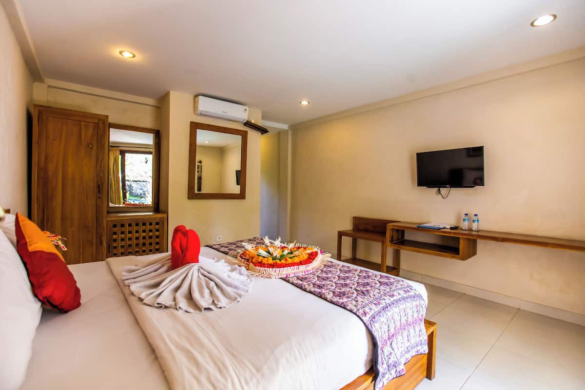A hotel room with a bed, a TV, a desk, and an air conditioning unit.