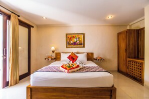 A hotel room with a bed, a painting on the wall, and a wooden wardrobe. - Asri Sari Villa Ubud (Ubud)
