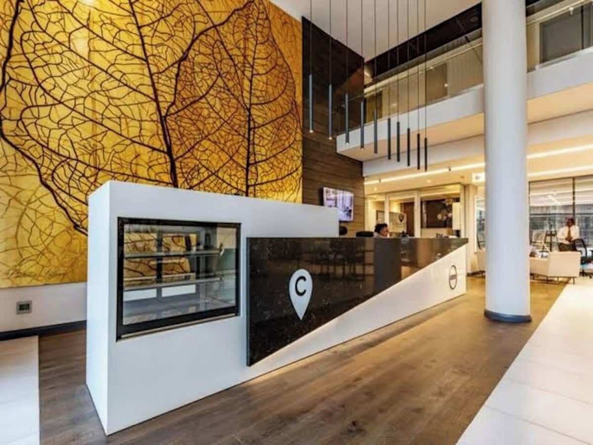 Un comptoir d’accueil moderne, orné d’un logo, avec un grand mur décoré d’une œuvre abstraite et un aménagement intérieur à plusieurs niveaux.